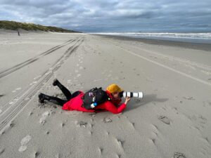 Jolanda Pikkaart liggend op het Amelandse strand om een zeehond te fotograferen